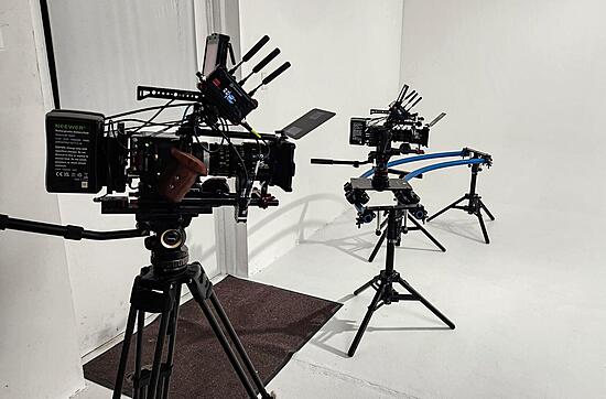 Two cinema cameras sit in a white cyclorama studio ready to be used.